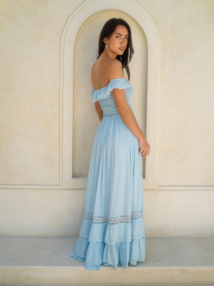 Woman wearing a light blue off-shoulder dress standing in front of an arched doorway.