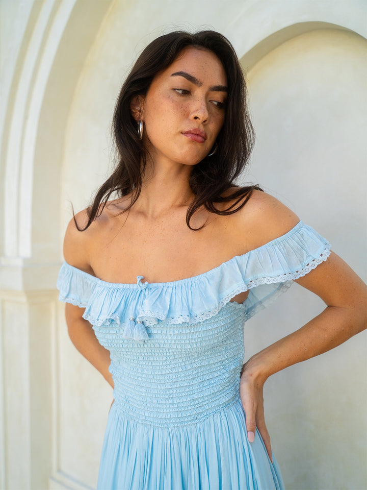 Woman wearing a light blue off-shoulder dress against a white wall.