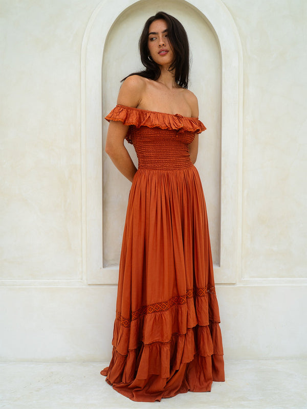 Woman wearing a rust-colored off-shoulder dress standing in front of a white archway.