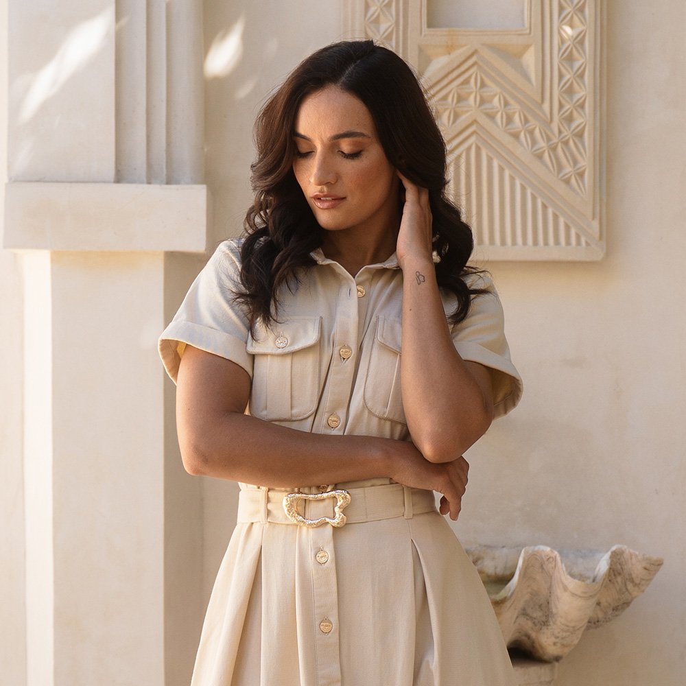 Woman in a beige dress standing against a decorative wall.