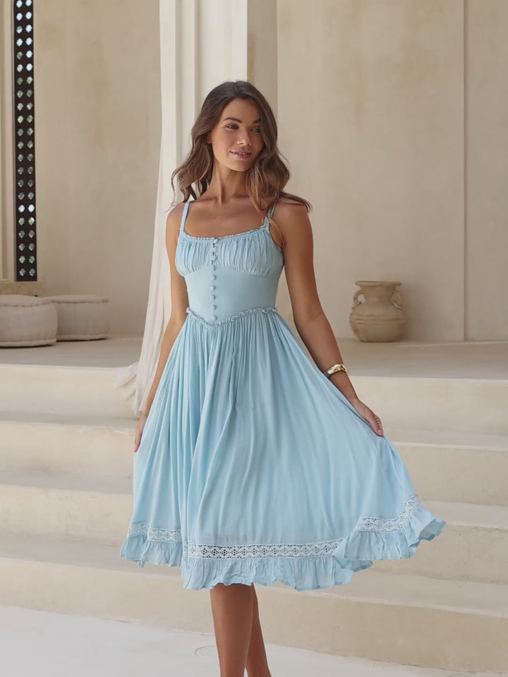 Woman in a light blue dress standing on steps with a neutral background