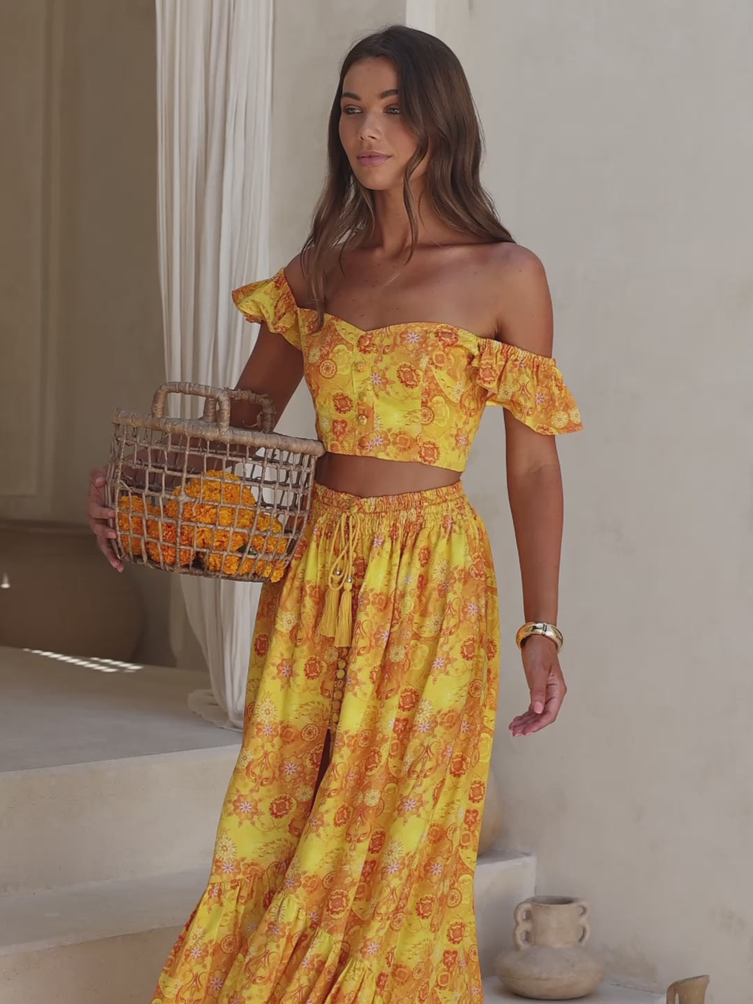 Woman in a yellow floral outfit holding a woven basket on stone steps.